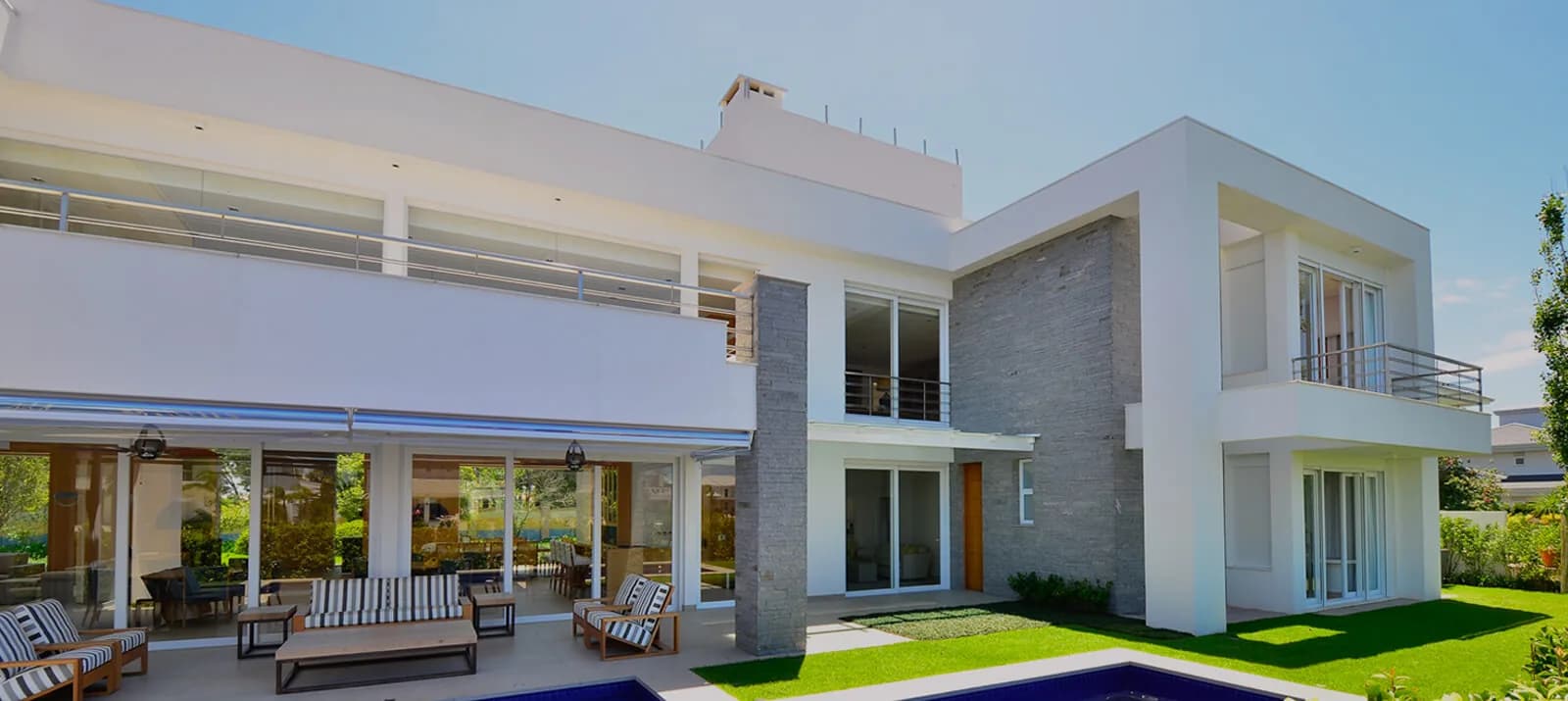 Casa branca de dois pavimentos com esquadrias amplas, varanda mobiliada e piscina