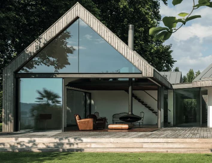 Casa com telhado de duas águas, fachada envidraçada, revestimento de madeira e deck