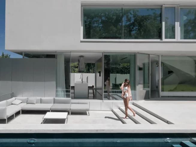 Casa de linhas minimalistas com esquadrias de vidro do piso ao teto, terraço com sofás e piscina
