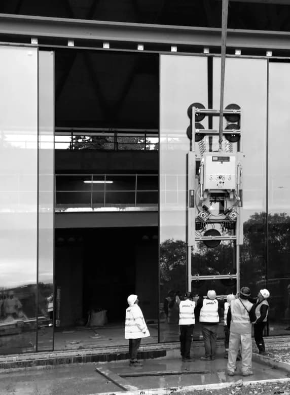 Equipe com capacetes e coletes instalando um grande painel de vidro com ventosa mecânica, em foto preto e branco
