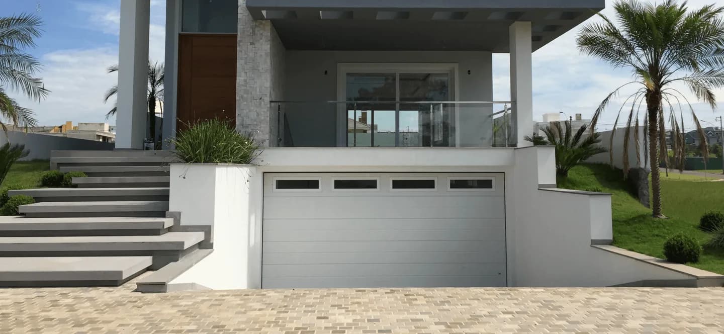 Fachada de residência com portão seccional de garagem branco, escada de acesso e palmeiras
