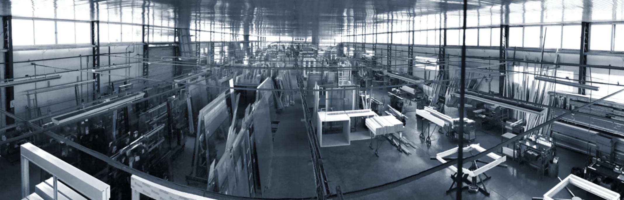 Panorâmica do interior do parque fabril da Esquadrias Prata, com máquinas e bancadas, em tom azulado