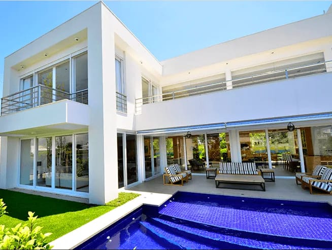 Casa branca com esquadrias de PVC brancas, varanda coberta e piscina azul