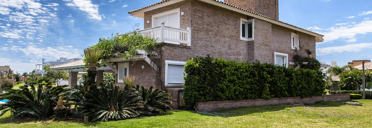 Casa de tijolos à vista com janelas de PVC brancas da Linha Capri, jardim gramado e palmeiras